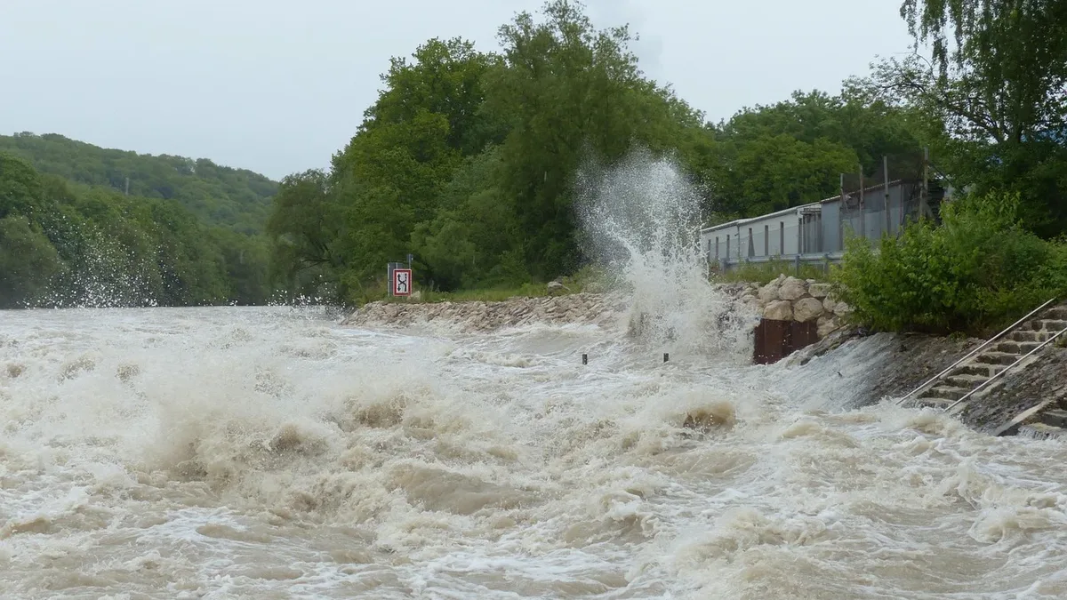 A river in flood, with a large amount of water overflowing its banks and causing a significant amount of debris to be washed away.